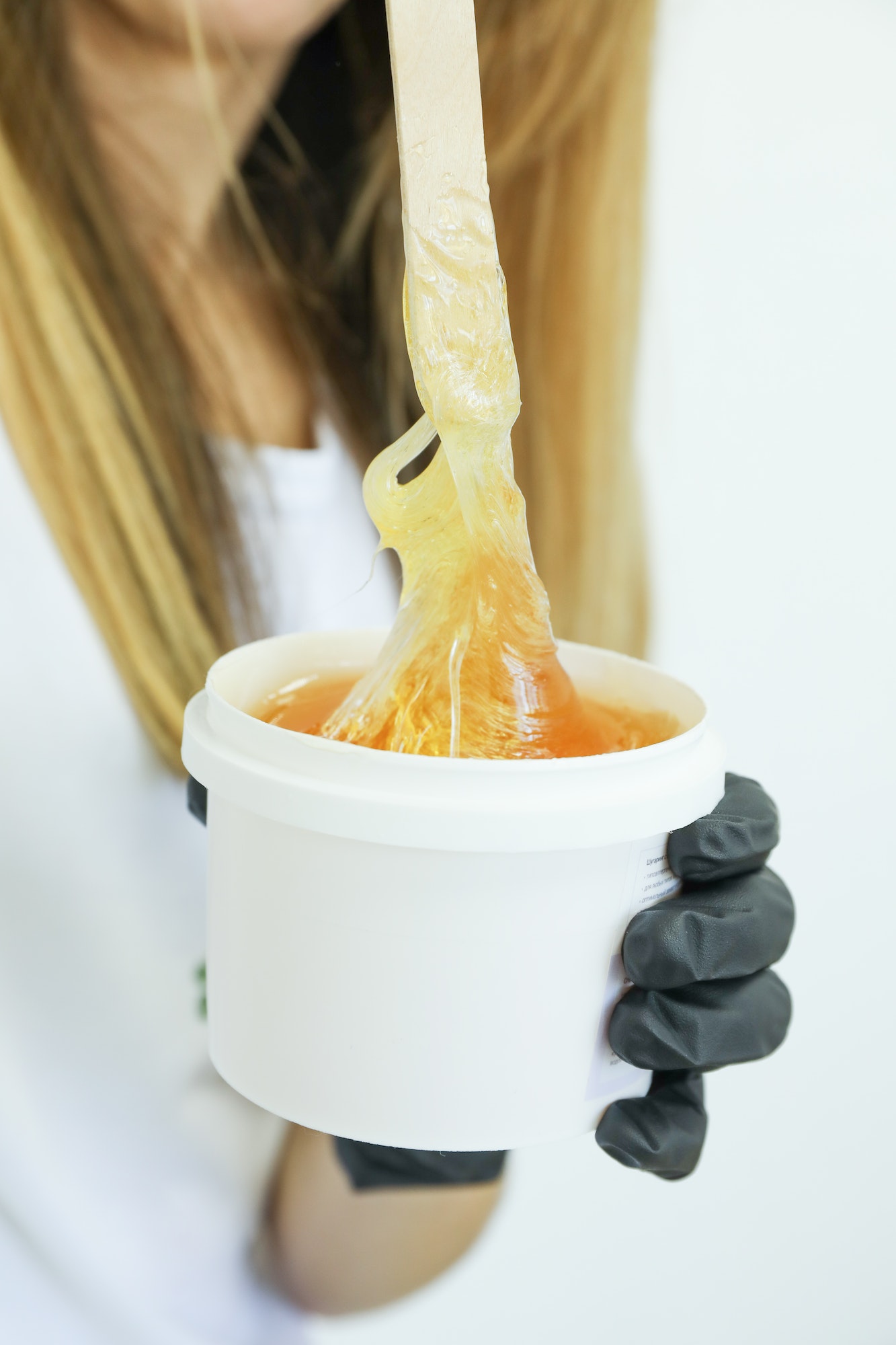 Woman holding liquid yellow paste for shugaring against white background, close up